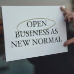 a person holding a sign that says open business as new normal
